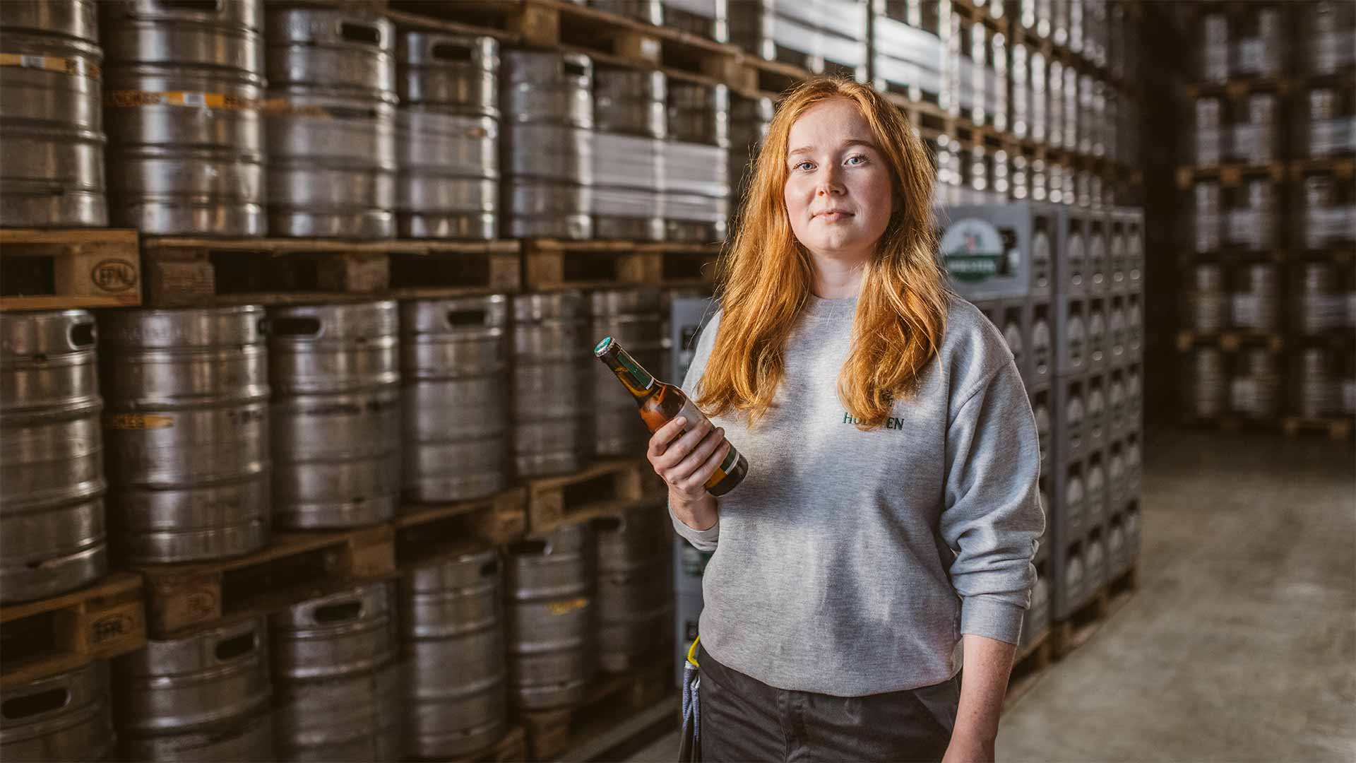 Holsten Prozessingenieurin Anna steht stolz vor Bierfässern im Lager